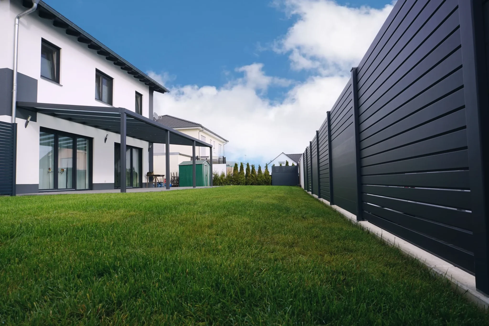 Weikum Überdachung - Ein Haus mit einem schwarzen Zaun und einem grasbewachsenen Hof.